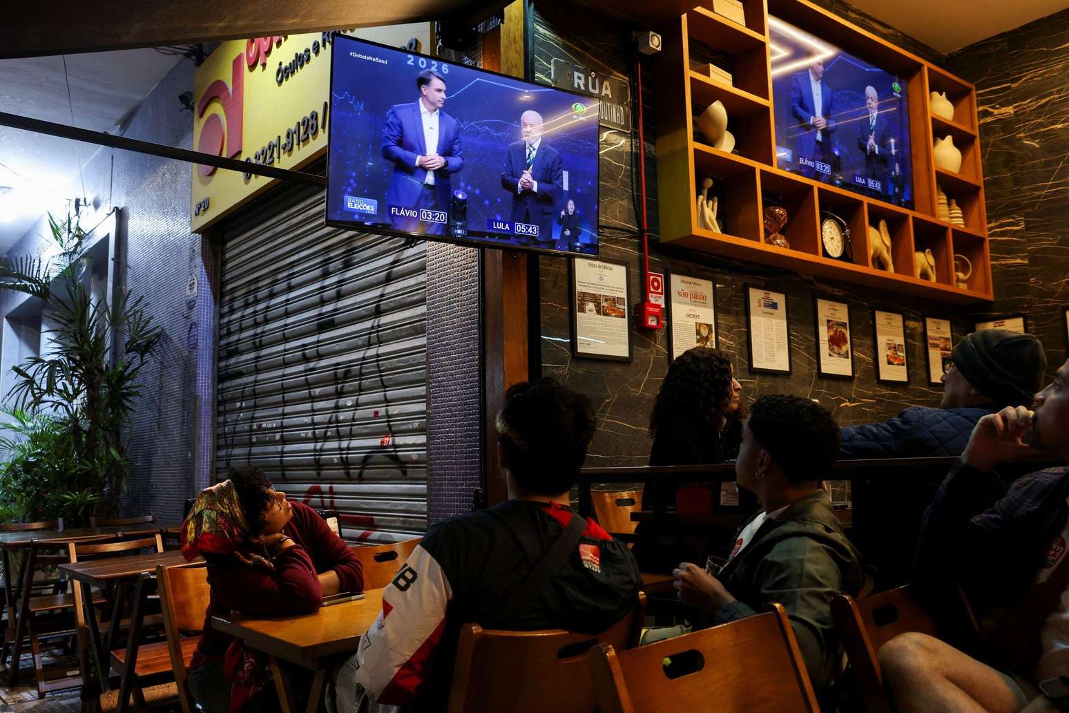 Pessoas assistem ao debate presidencial na televisão entre o candidato à presidência do Brasil, Flávio Bolsonaro, do Partido Liberal (PL), e o presidente Luiz Inácio Lula da Silva, do Partido dos Trabalhadores (PT), em São Paulo, Brasil, em 18 de outubro de 2026